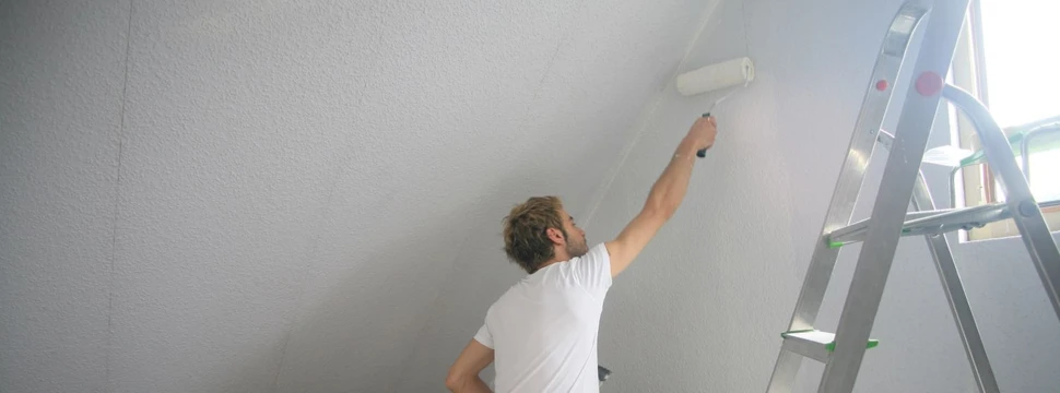 Mann mit Leiter streicht Innenbereich eines Hauses