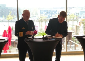 Zwei Menschen vor einem Tisch, auf dem Unterlagen liegen, die unterschrieben werden sollen