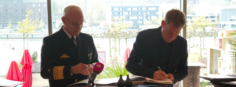 Zwei Menschen vor einem Tisch, auf dem Unterlagen liegen, die unterschrieben werden sollen