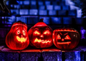 Drei beleuchtete Halloween-Kürbisse schaffen gruselige Atmosphäre in der nächtlichen Stadt. Drei leuchtende Halloween-Kürbisse mit gruseligen Gesichtern vor blau beleuchteter Stadtkulisse bei Nacht.