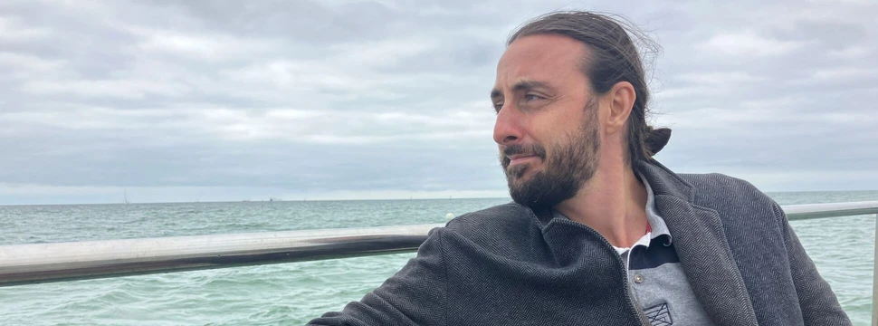 Ein Mann auf einer Bank mit Wasser und Wolken im Hintergrund