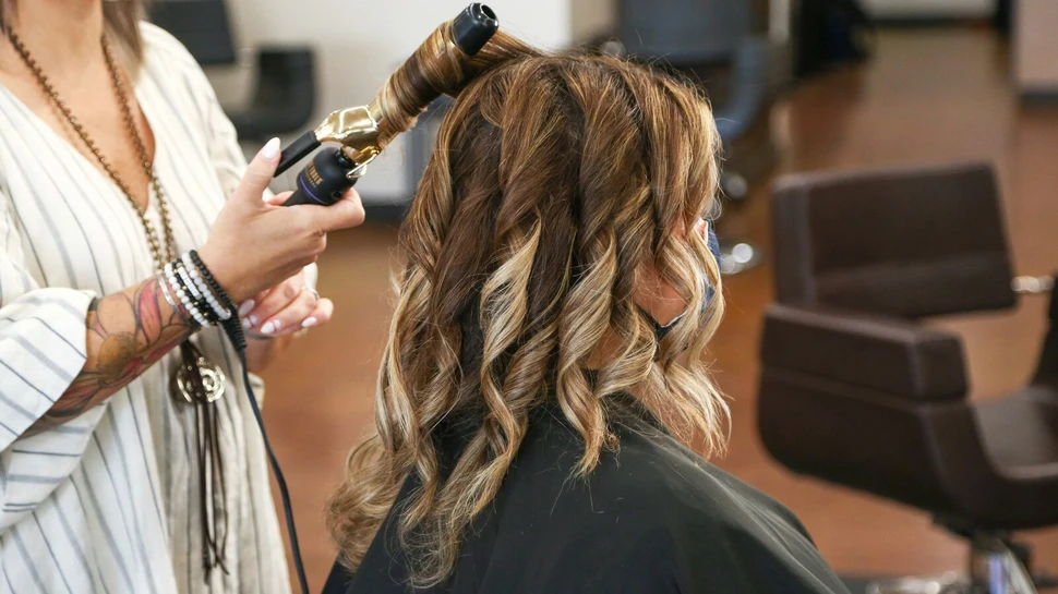 Frau hat Lockenstab in der Hand und macht einer Frau Locken damit