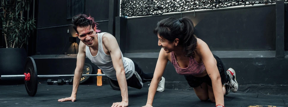 Zwei Menschen, die gerade Sport in einem Raum mit einem schwarzen Boden machen