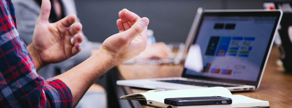 Mann sitzt vor einem Laptop und gestikuliert mit den Händen
