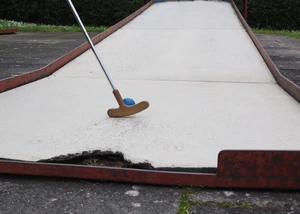 Ein Schläger, der einen Minigolfball auf einer Bahn berührt