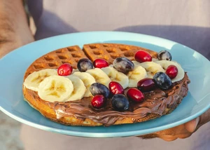 Eine Person hält einen Teller. Auf dem Teller ist eine Waffel mit Obst und Schokolade