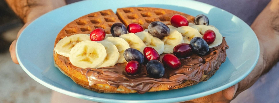 Eine Person hält einen Teller. Auf dem Teller ist eine Waffel mit Obst und Schokolade