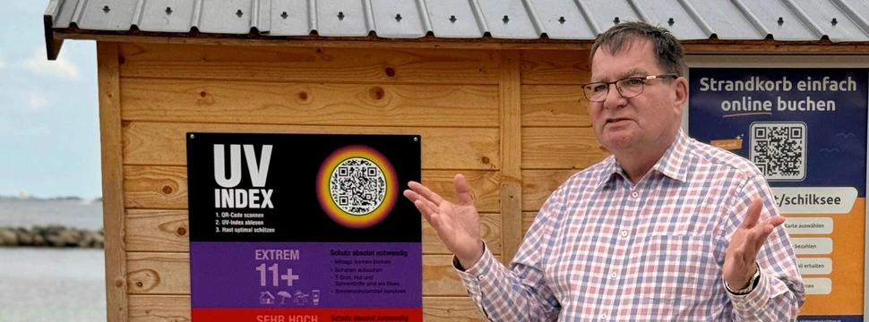 Sonnenschutz ist eine wichtige Maßnahme in der Hautkrebsvorbeugung Mann vor einer Infowand am Strand