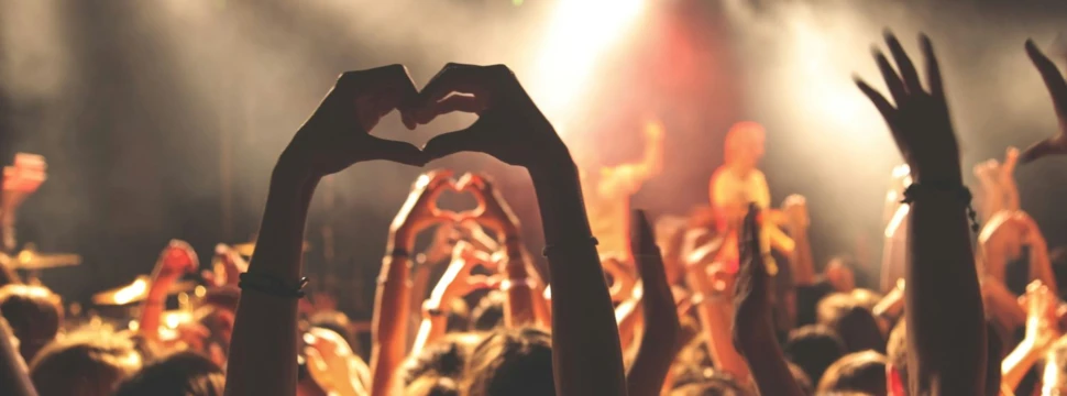 nach oben gereckte Arme vor einer Konzertbühne