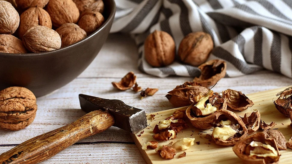 Walnüsse auf einem Holzbrett, die mit einem Hammer aufgebrochen werden