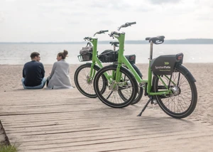 Zwei Menschen sitzen am Strand, im Vordergrund grüne Leihfahrrädern