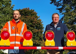 Tiefbauamtsleiter Peter Bender und Projektleiter Henning Bergmann vor der neuen Schranke im Skagenweg Zwei Männer, davon einer in einer orangenen Weste mit der Aufschrift "Tiefbauamt" und der andere in einer dunkelblauen mit der Aufschrift "Kiel", vor einer Schranke im Kieler Stadtteil Mettenhof
