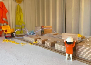 Eine Playmobilfigur, die vor mehreren Holzkötzen steht und an denen "arbeitet"