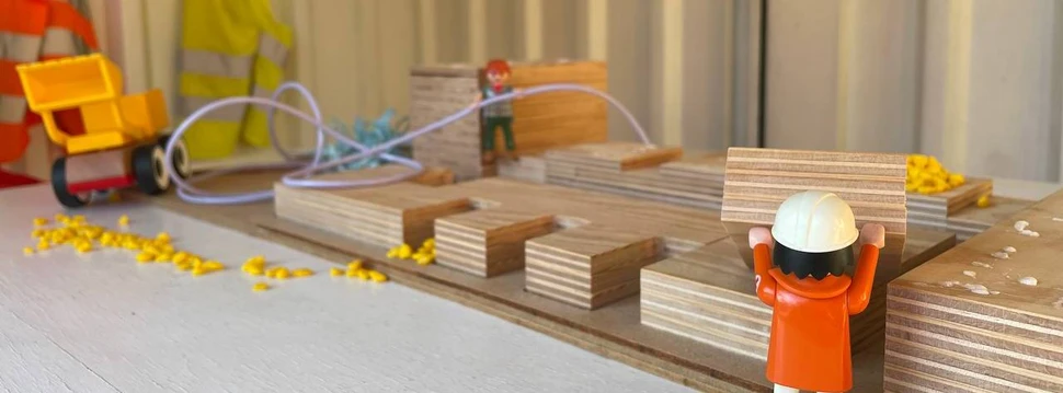 Eine Playmobilfigur, die vor mehreren Holzkötzen steht und an denen "arbeitet"