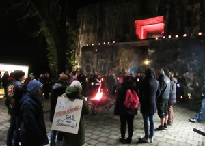 Mehrere Menschen, die vor einem Feuer vor dem beleuchteten Flandernbunker an die Opfer des Nationalsozialismus erinnern