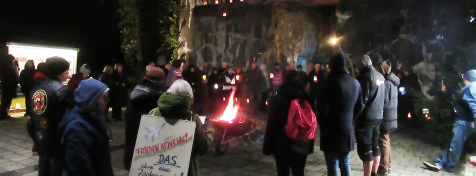 Mehrere Menschen, die vor einem Feuer vor dem beleuchteten Flandernbunker an die Opfer des Nationalsozialismus erinnern