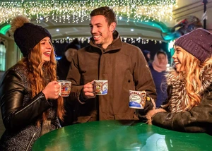 zwei Frauen mit Mütze und ein Mann, alle haben Becher mit Glühwein in der Hand