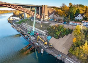 Ein Bagger und ein Kran unterhalb der Levensauer Hochbrücke mit dem Nord-Ostsee-Kanal im Hintergrund