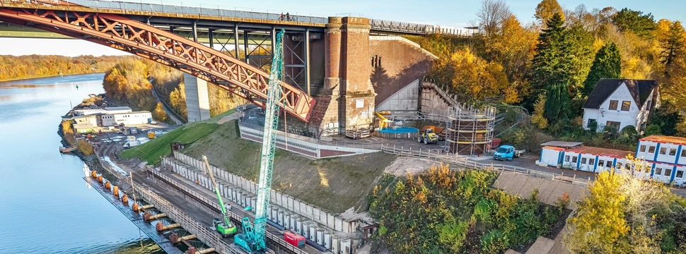 Ein Bagger und ein Kran unterhalb der Levensauer Hochbrücke mit dem Nord-Ostsee-Kanal im Hintergrund