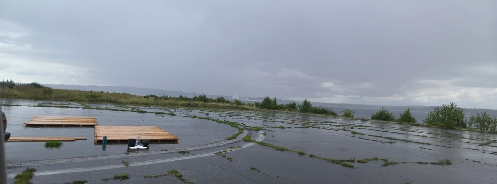 Zusammengebaute Holzplanken, die den Boden des Floßes bilden sollen, wenn diese einmal alle zusammengebaut sind, auf Betonboden mit der Kieler Förde im Hintergrund