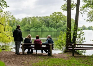 Erholung an einem Fluss in Mittelholstein Vier Menschen auf einer Bank mit einem Fluss und Bäumen im Hintergrund