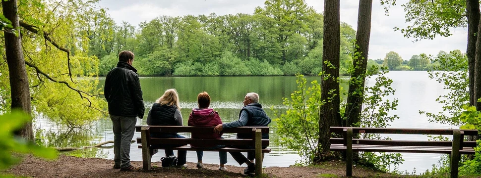 Vier Menschen auf einer Bank mit einem Fluss und Bäumen im Hintergrund