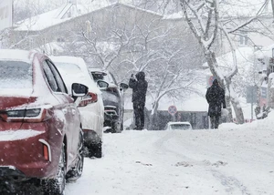 Mehrere zugeschneite Autos auf einer Straße, die von Menschen vom Eis befreit werden