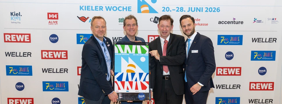 Vier Männer stehen vor einer Kieler Woche Werbewand und halten das neue Kieler Woche Plakat in den Händen