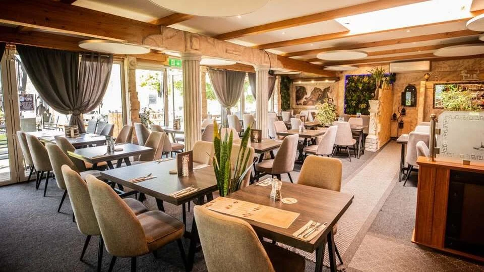 Das Restaurant Athen von Innen Ein Raum mit Lampen, weißen Stühlen und Tischen mit Tischdeko