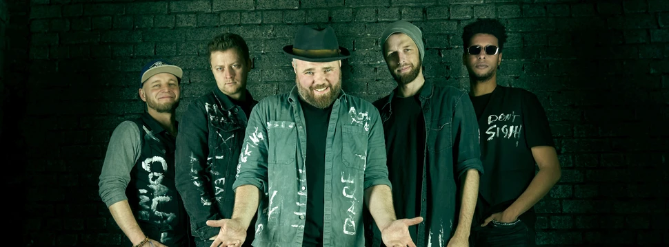 Vier Menschen aus einer Band in verschiedenen Posen vor einer Wand