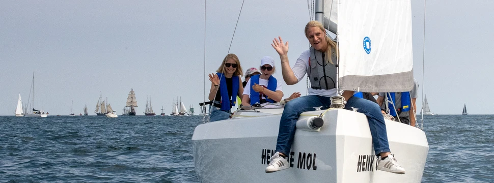 Ein Segelboot auf der Kieler Förde mit Menschen darauf und mit weiteren Booten im Hintergrund