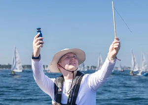 Ein Mann mit einem weißen Hut auf dem Kopf vor der Kieler Förde mit mehreren Schiffen im Hintergrund