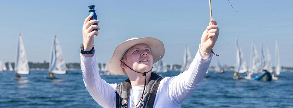 Ein Mann mit einem weißen Hut auf dem Kopf vor der Kieler Förde mit mehreren Schiffen im Hintergrund